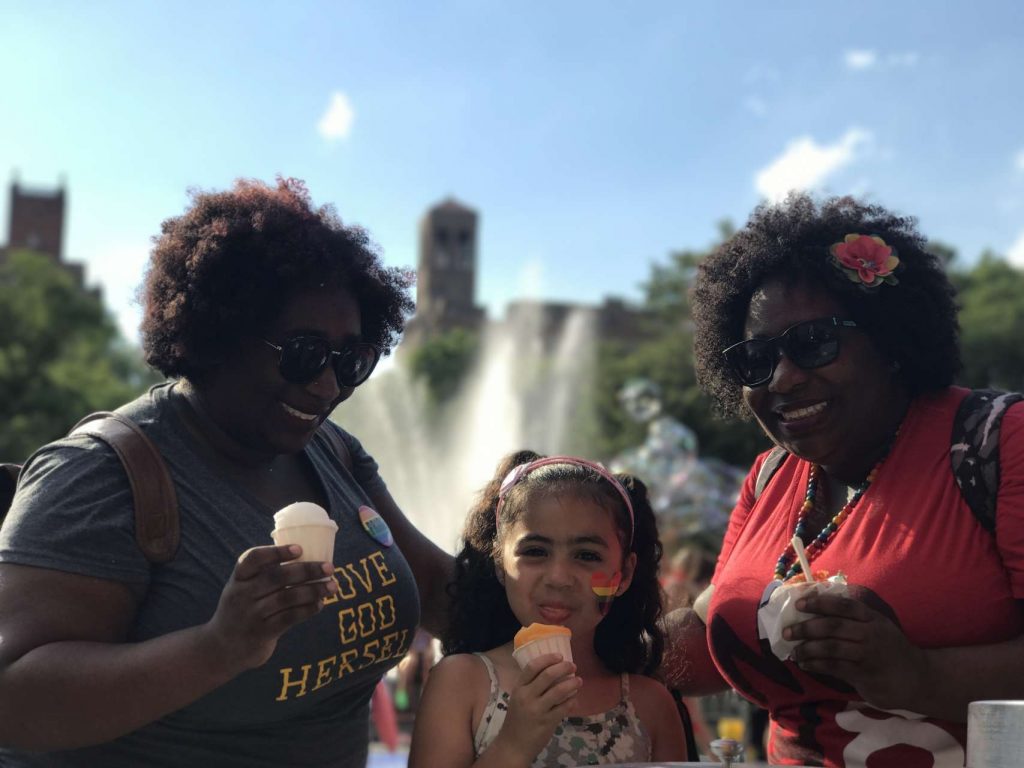 India Jolie girl sticking out tongue eating ices standing in between two women twins with curly afros eating Indias Italian Ice