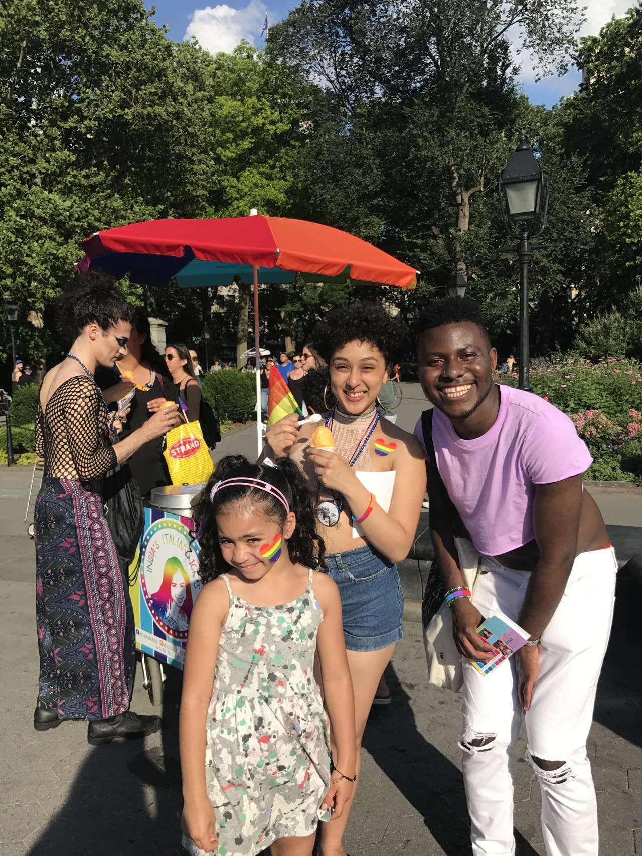 girl with rainbow heart sticker India Jolie standing in front of Italian Ice cart and other people eating and buying Italian Ices in the park