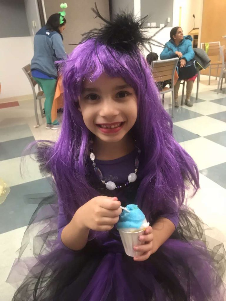 Girl in monster high purple wig costume eating blue italian ice